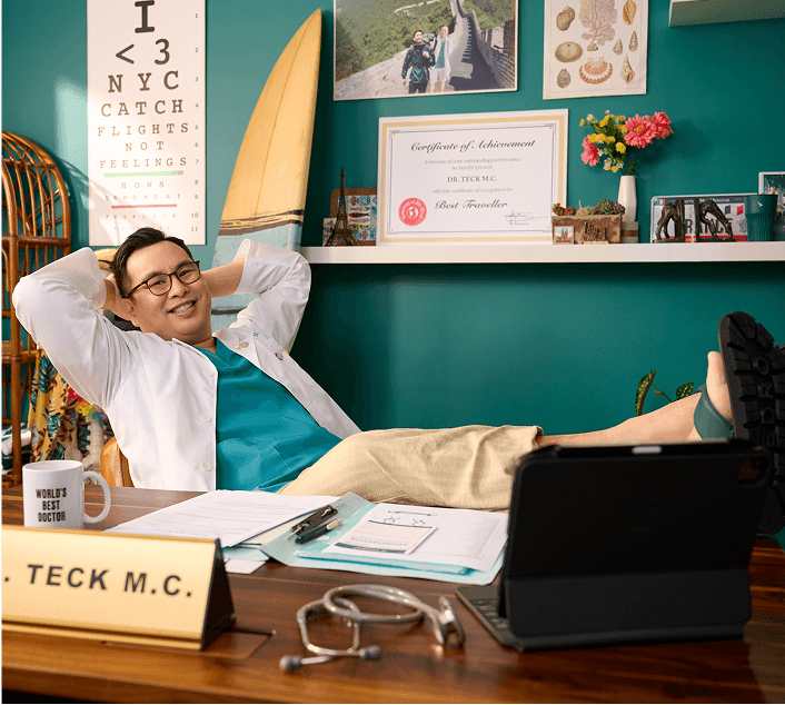 Dr. Teck M.C. smiling, leans back in his chair with feet on the desk next to a "World’s Best Doctor" mug.